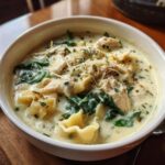 Close-up of a bowl of white chicken lasagna soup with shredded chicken, spinach, pasta, and grated cheese.