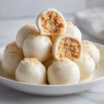 A stack of white chocolate coated sugar cookie truffles, with two cut in half showing the crumbly center.