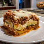 A close-up shot of a hearty slice of zucchini lasagna layered with meat sauce, ricotta, and melted mozzarella cheese.
