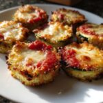 Close-up of several golden-brown zucchini pizza bites topped with melted mozzarella and marinara sauce.