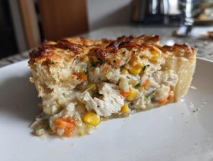 Close-up of a hearty slice of chicken pot pie showing creamy filling with chicken, carrots, and corn under a golden crust.
