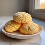 A stack of three bright yellow, sugar-coated cake mix cookies with cracked tops resting on a small ceramic plate.