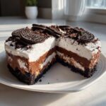 A slice cut from a rich Mississippi Mud Pie showing four distinct layers, topped with whipped cream and whole Oreos.