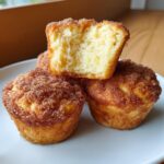 Three air fryer cinnamon sugar french toast muffins stacked on a white plate, one cut open showing the fluffy interior.