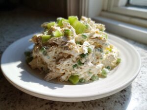 A mound of creamy chicken salad recipe mixed with celery and green onions, served on a white plate.