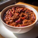 Close-up of a rich, hearty bowl of chili recipe featuring ground meat and kidney beans in a thick red sauce.