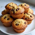 A close-up stack of freshly baked mini chocolate chip muffins with golden brown tops.