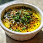 Close-up of an amazing olive oil bread dip, rich yellow oil topped with fresh green herbs and red pepper flakes.