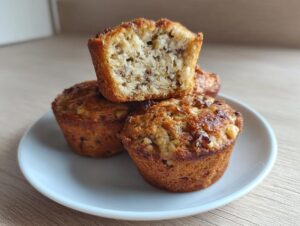A stack of three golden brown protein muffins, one cut in half showing the moist interior texture.