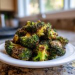 A close-up of a pile of perfectly crispy roasted broccoli, seasoned with spices, served on a white plate.