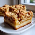 A close-up, appetizing shot of a single square of apple pie bars showing the thick apple filling and crumb topping.