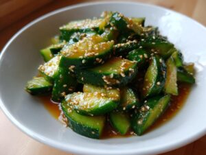 Close-up of vibrant green, smashed cucumber pieces coated in a savory dressing and topped with toasted sesame seeds in an asian cucumber salad.