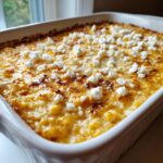 Close-up of a creamy, baked corn elote dip topped with crumbled white cheese in a white baking dish.