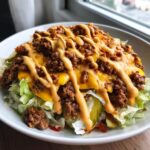 A close-up of a big mac salad featuring shredded lettuce, ground beef, melted cheese, pickles, and a generous drizzle of special sauce.