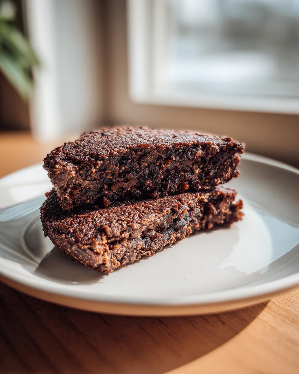 Close-up of two stacked, dark brown, textured slices of a homemade black bean burger patty on a light plate.