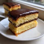 Close-up of a layered slice of boston cream pie showing cake, pastry cream, and chocolate ganache.