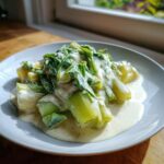 Close-up of tender braised leeks with cream and white wine sauce served on a white plate.