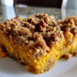 A close-up, appetizing view of a serving of butternut squash casserole topped with a thick, crumbly pecan streusel topping.