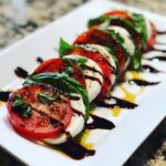 Close-up of a beautiful caprese salad featuring alternating slices of tomato, mozzarella, and basil drizzled with balsamic glaze.