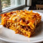 A thick, cheesy slice of baked Frito Pie casserole layered with seasoned ground meat and melted cheddar cheese.
