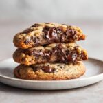 A stack of three perfectly chewy chocolate chip cookies with melted chocolate centers.
