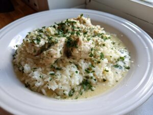 A bowl of chicken scampi with garlic parmesan rice, topped generously with fresh chopped parsley.