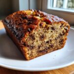 A close-up of a freshly baked slice of chocolate chip banana bread with a dark, caramelized crust.