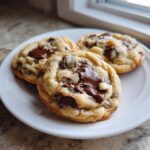 Three soft, gooey chocolate chip cookies made with vanilla instant pudding on a white plate.