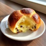 A cross-section of a chocolate chip vanilla custard brioche showing rich, flowing vanilla custard and chocolate chips inside.