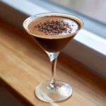 A creamy, dark chocolate martini in a stemmed glass, garnished with chocolate shavings.
