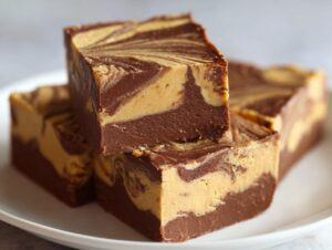Three thick squares of marbled chocolate peanut butter fudge stacked on a white plate.