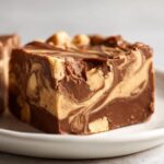 A close-up of a thick square of swirled chocolate peanut butter fudge, topped with peanuts.