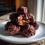 A stack of rich, dark chocolate rice krispie balls, with one clearly showing the crispy interior.