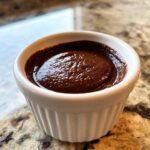 Close-up of thick, dark chocolate sauce for churros served in a small white fluted ramekin.