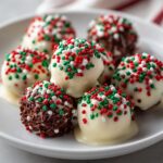 Close-up of several christmas chocolate rice krispie balls, some coated in white chocolate and red/green/white sprinkles.