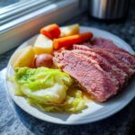 A plate featuring slices of tender corned beef and cabbage, potatoes, and carrots, ready to eat.
