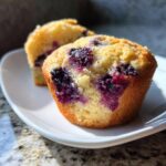 Close-up of a fluffy cottage cheese blueberry muffin showing bright purple berries baked into the golden crumb.