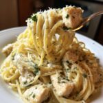 A close-up shot of creamy chicken pasta being lifted high on a fork, topped with Parmesan cheese and parsley.