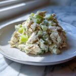A generous scoop of creamy chicken salad recipe mixed with chopped celery, served on a white plate.