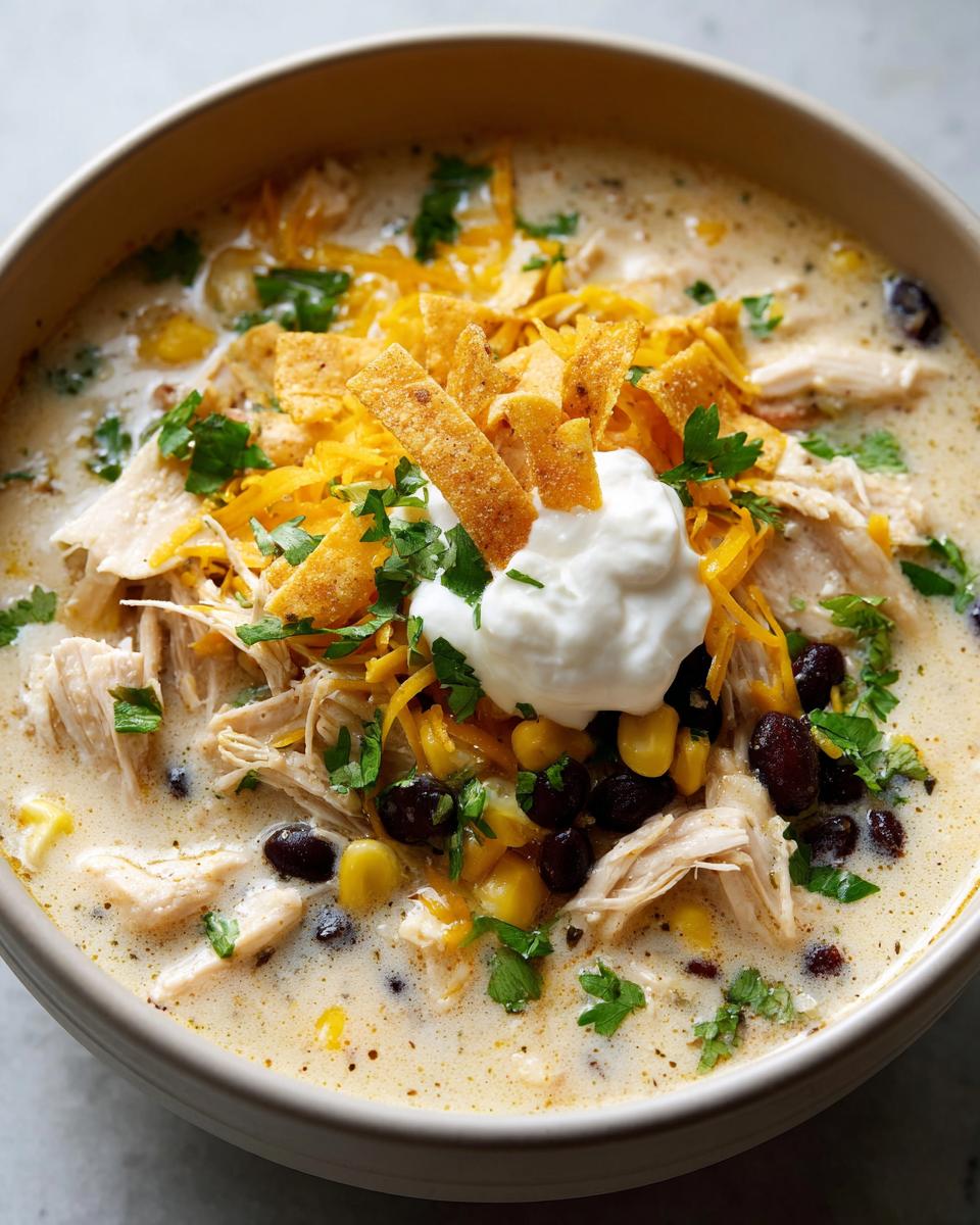 Close-up of creamy chicken tortilla soup crock pot topped with shredded chicken, cheese, black beans, and sour cream.