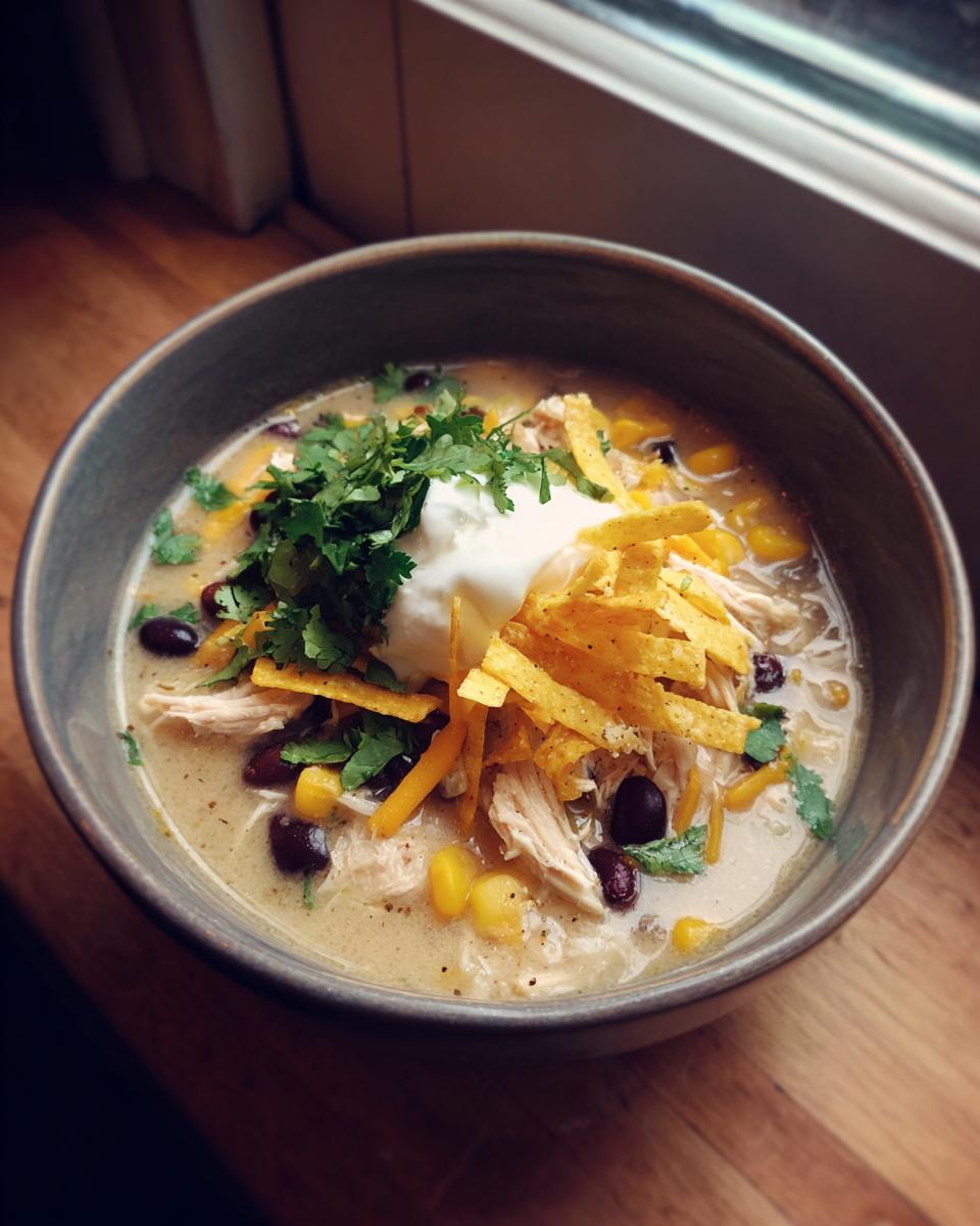 A bowl of creamy chicken tortilla soup crock pot recipe, topped with sour cream, cilantro, cheese, and tortilla strips.