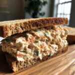 A thick, creamy seafood salad sandwich made with toasted whole wheat bread, generously filled with seafood salad.