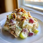 A mound of creamy Waldorf salad featuring grapes, chopped apples, and topped generously with whole walnuts.