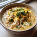A close-up of a bowl of creamy white chicken chili recipe, topped with shredded cheddar cheese and fresh cilantro.