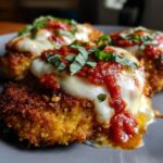 Close-up of three golden, crispy chicken parmesan recipe portions topped with melted mozzarella and rich tomato sauce, garnished with fresh basil.