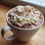 Close-up of a mug filled with rich crockpot hot chocolate topped high with whipped cream and a dusting of cinnamon.
