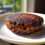 Close-up of a perfectly seared, dark brown easy black bean burger patty resting on a white plate.