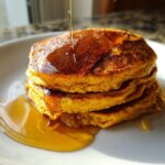 Close-up of a stack of fluffy pumpkin pancakes being drizzled with golden syrup.
