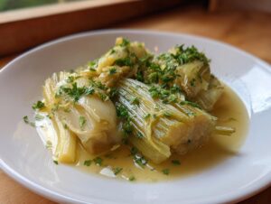Close-up of tender french braised leeks served in a light broth and topped with fresh chopped parsley.
