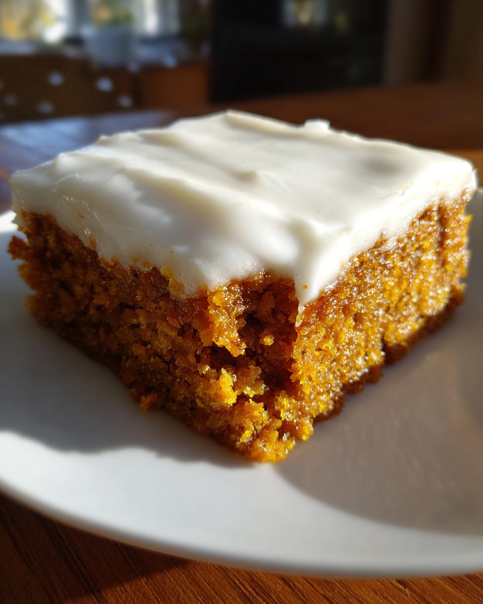 A moist, square slice of orange pumpkin bars topped with thick white cream cheese frosting.